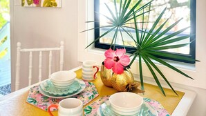 Una mesa de comedor con mantel amarillo, sillas blancas y una ventana con vistas a zonas verdes.