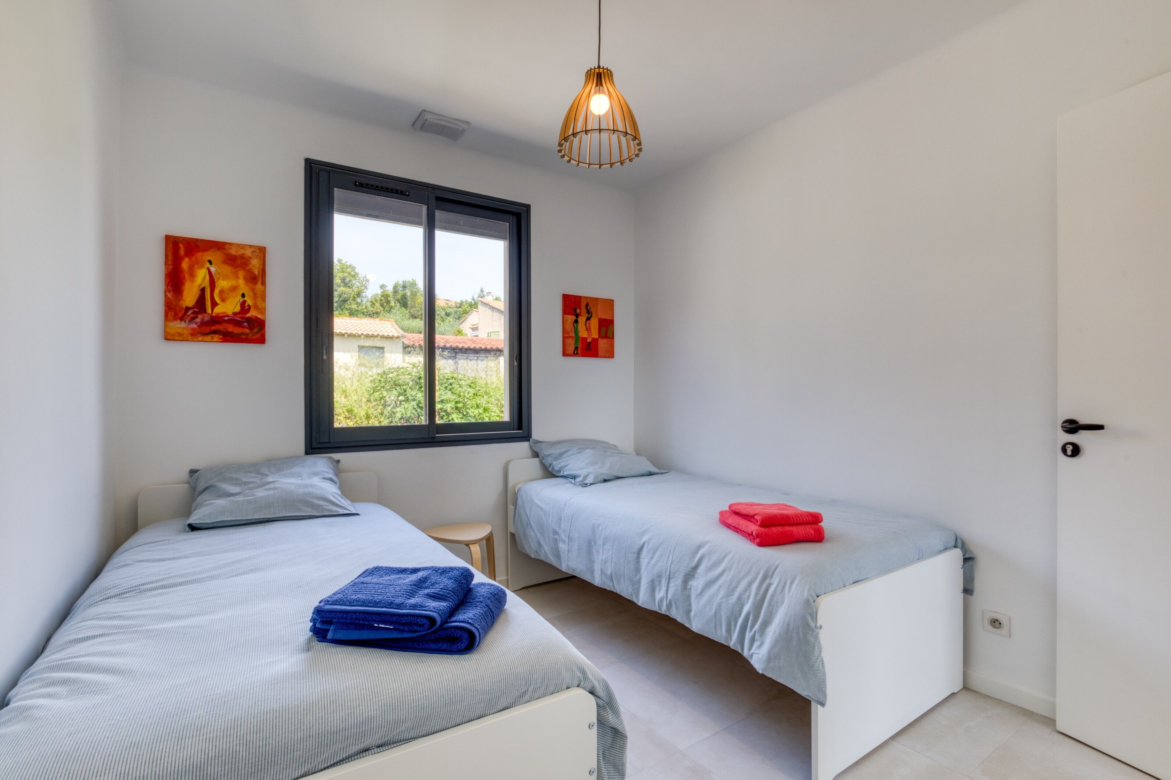 A bedroom with two beds, a window, and artwork on the walls.