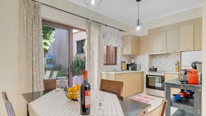 Une cuisine moderne avec un coin repas, comprenant une table avec une bouteille et des verres, un plan de travail avec des appareils électroménagers et une vue sur l’extérieur.