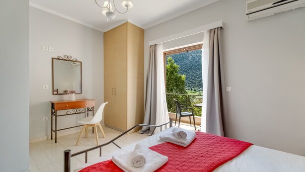 Une chambre à coucher comprenant un lit, un bureau, une chaise, un miroir et un balcon avec vue.