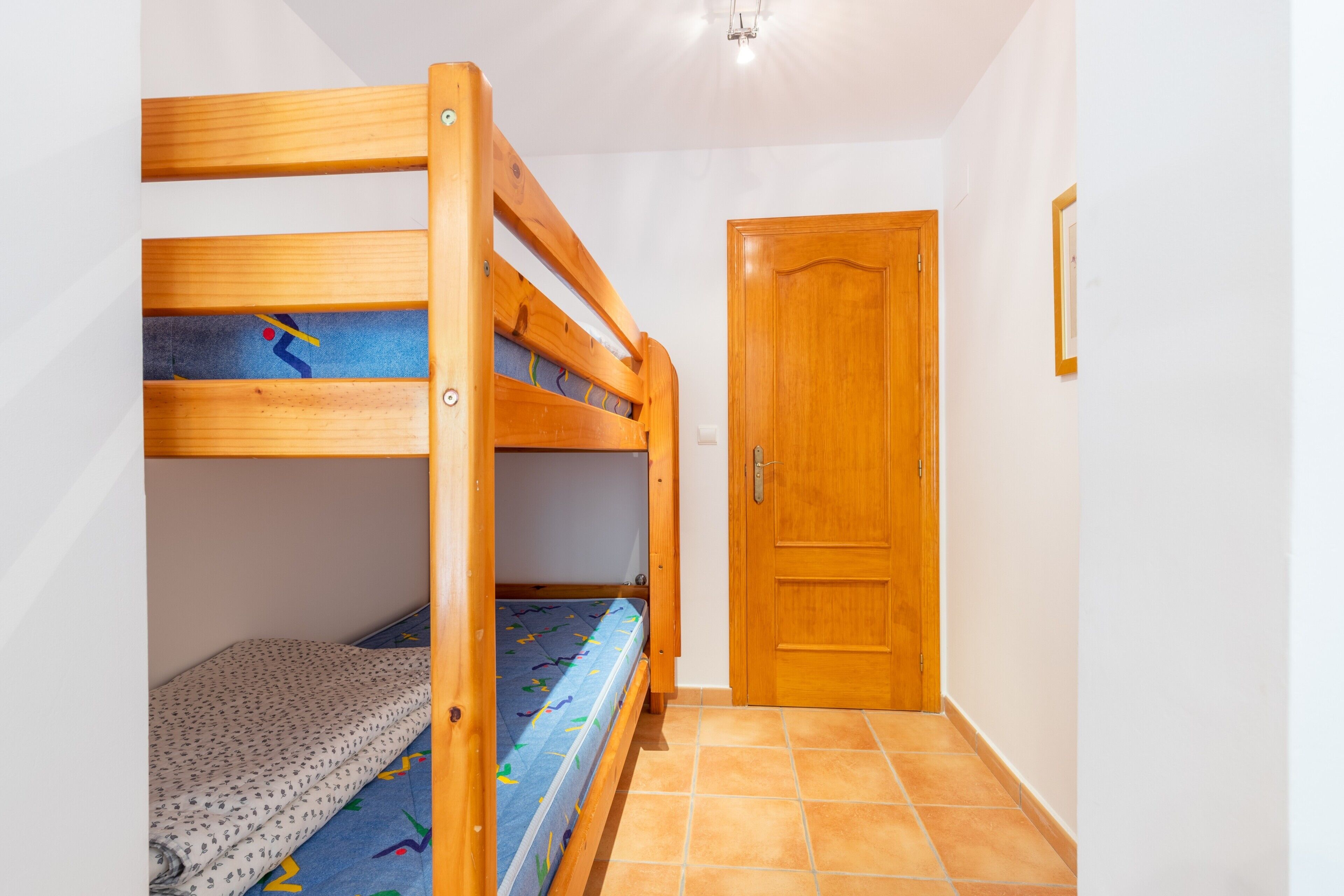 Una cama litera con un colchón estampado, una puerta de madera y un suelo de baldosas.