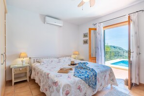 A bedroom with a bed, two bedside tables, a lamp, a window with curtains, and a view of a swimming pool. - Holiday Villa Near Denia with Mountain View, Pool & Wi-Fi (L'Atzúbia)
