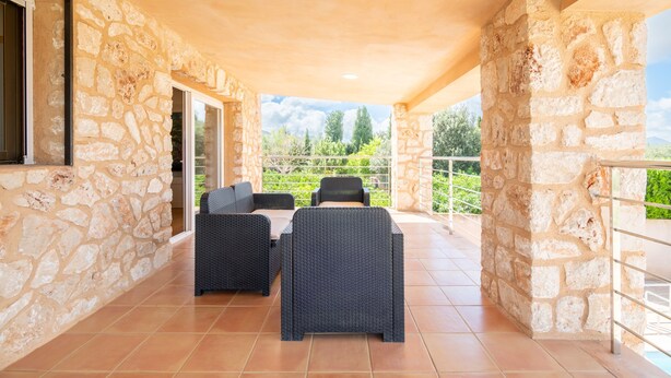 A stone-walled patio with a table and chairs, a glass door, and a view of greenery.