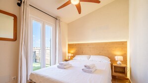 A hotel room with a bed, a ceiling fan, a nightstand with a lamp, and a view of the outdoors.