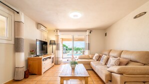 A living room with a sofa, TV, wooden table, and a view to the outside.