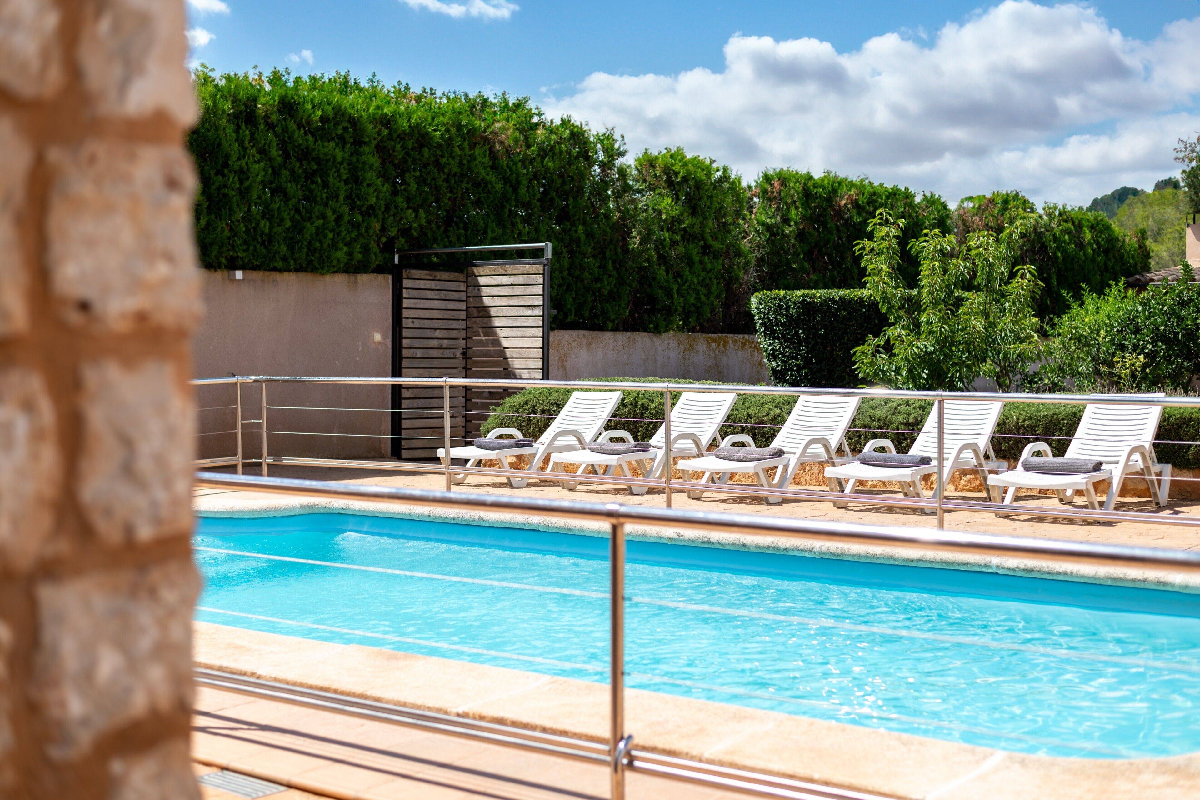 Una piscina con sillones de descanso, un muro de piedra y un seto al fondo.