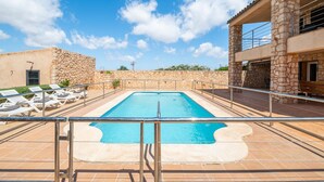 A swimming pool with lounge chairs, stone walls, and a clear sky.