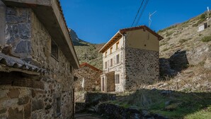 A narrow stone pathway leading to a traditional stone building with a tiled roof, surrounded by hills.