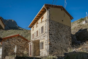 A two-story stone building with a red-tiled roof, a balcony, and a stone wall.