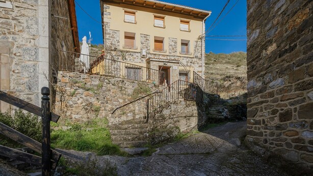 A narrow stone pathway leading to a building with a wooden staircase and a balcony.
