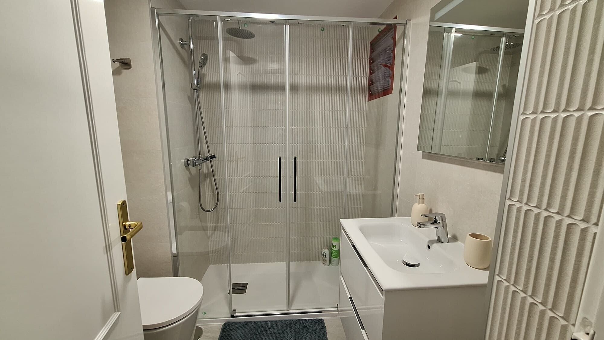 A bathroom with a shower, toilet, sink, and a mirror.