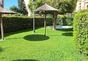 Un jardí ben cuidat amb un porxo de palla, una petita font i un arbustos perfectament podats.