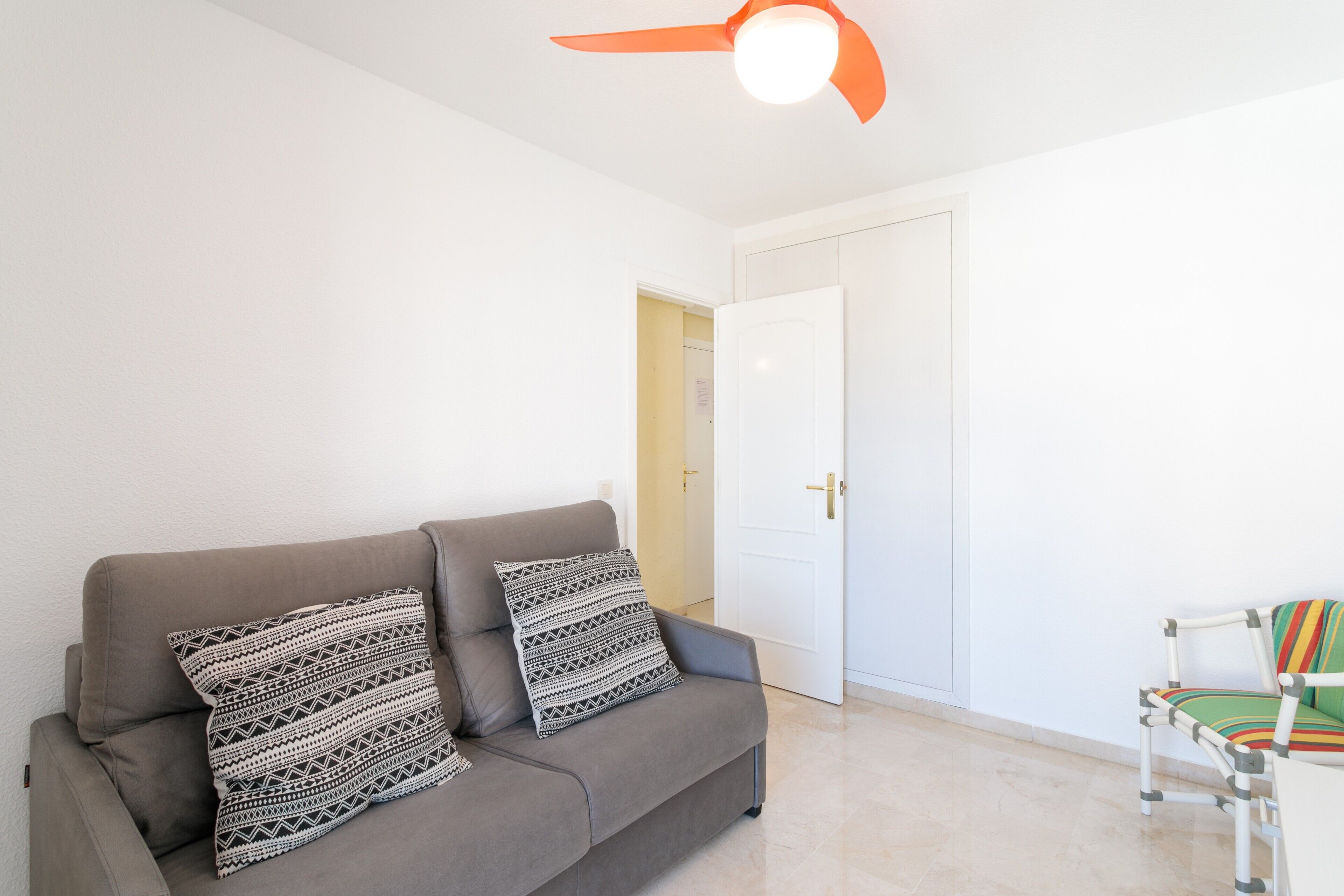 Una stanza con un divano grigio, cuscini decorati, una porta bianca e una sedia con un cuscino a righe.