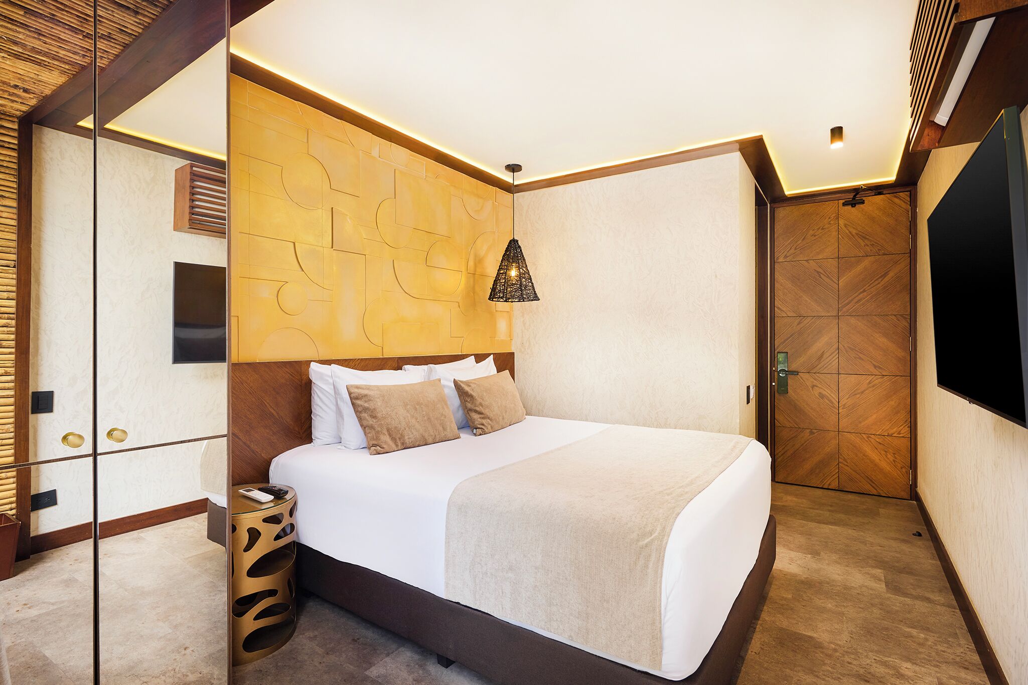 A modern hotel room with a large bed, a TV, a wooden accent wall, and a unique pendant light.