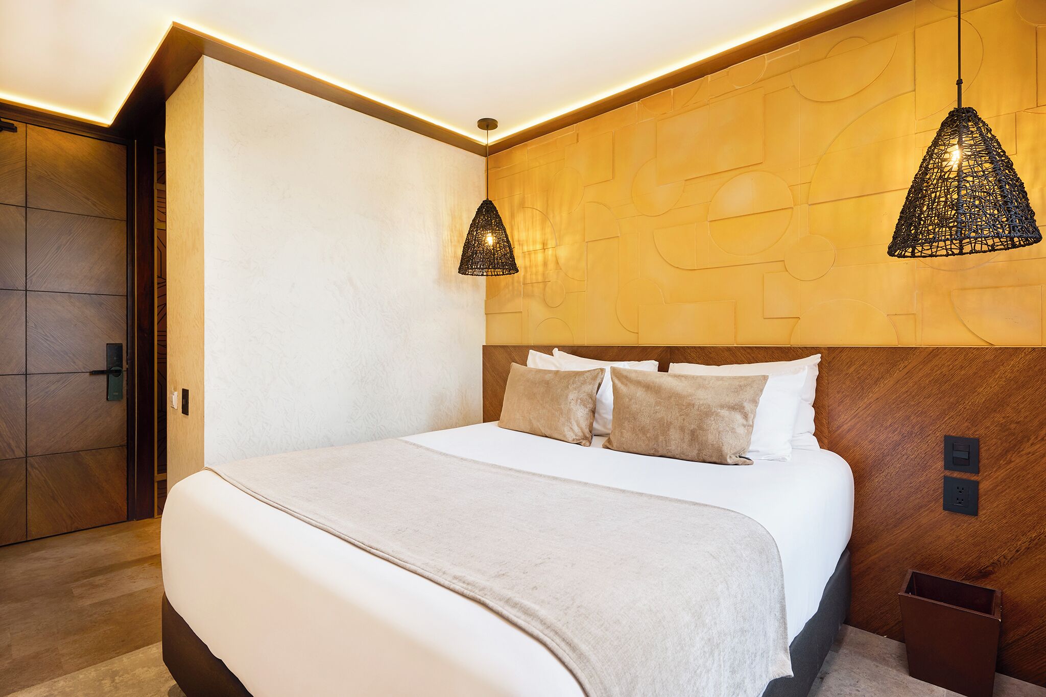 Ett modernt hotellrum med en stor säng, ett träpanelat sänggavel och två hängande pendellampor.