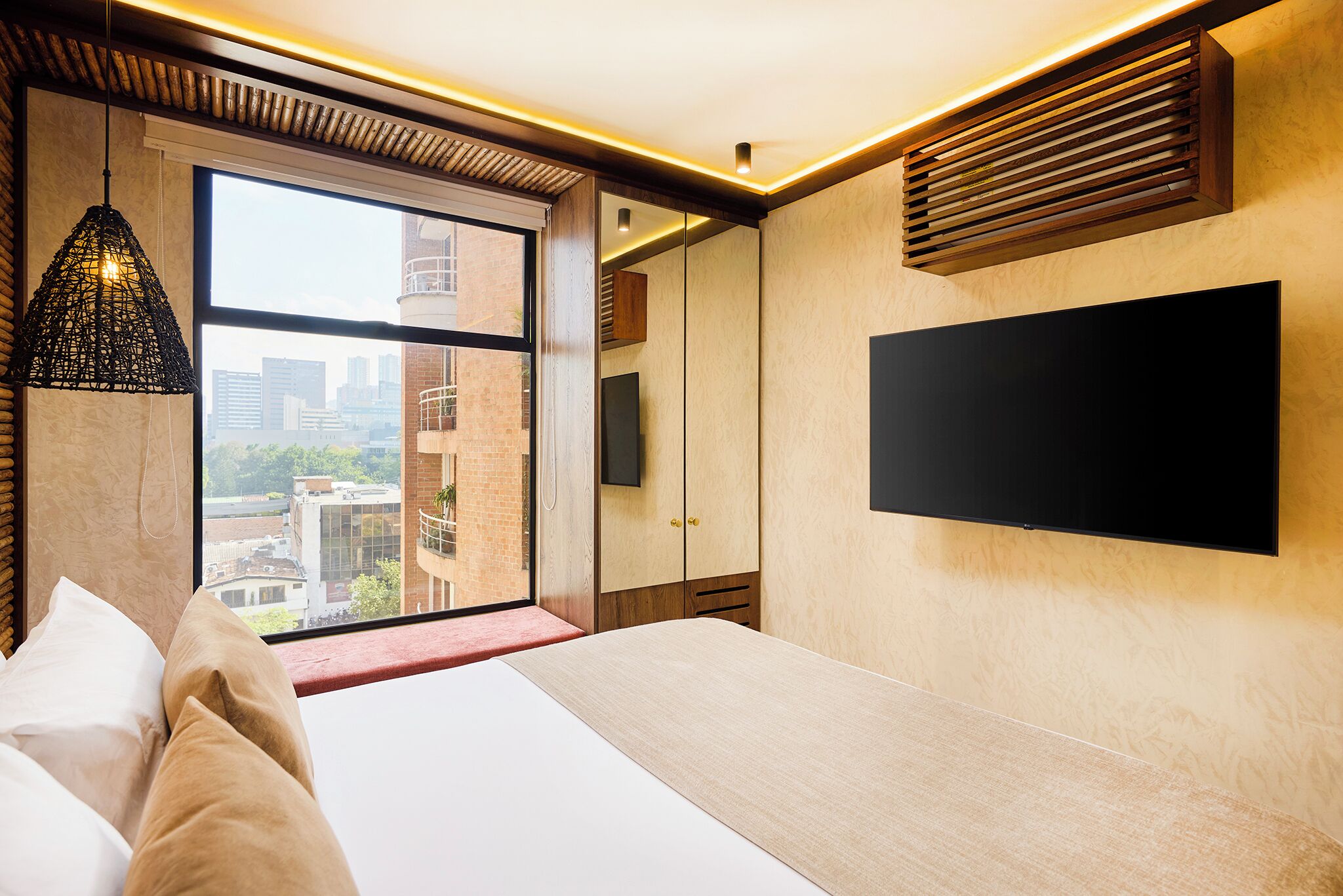 Un hotel moderno con una cama grande, un televisor montado en la pared y vistas a la ciudad a través de un ventanal.