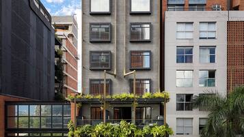 Un edificio de varias plantas con diseño moderno, con balcones con plantas, ventanas amplias y fachadas combinadas de ladrillo y hormigón.