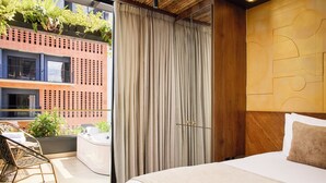 A hotel room with a bed, a bathroom, a balcony with plants, and a view of a building with a red facade. - Golden Valley Hotel (Medellín)