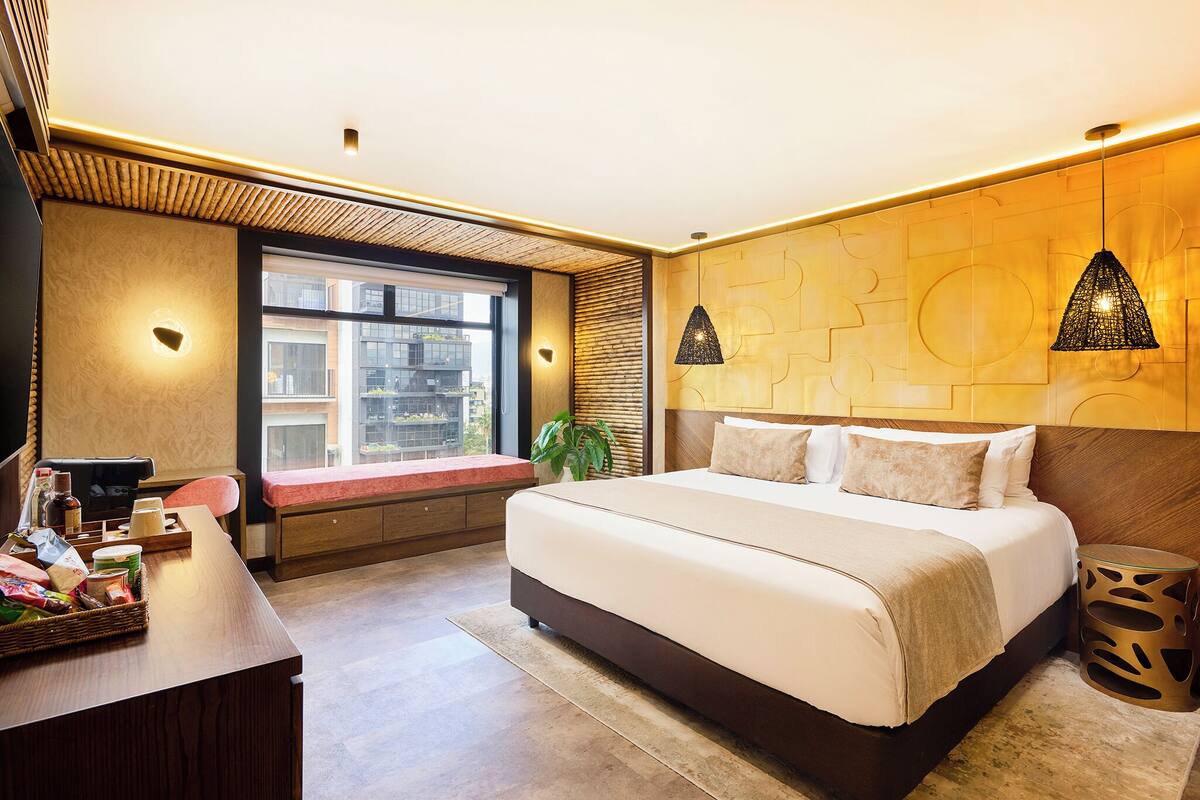 A modern hotel room with a large bed, a desk, and a window with a view of buildings.
