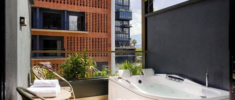 Un balcón con jacuzzi, sillas de mimbre y vista a un edificio con balcones.