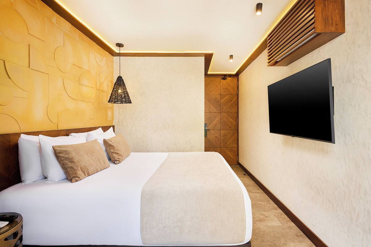 A modern hotel room with a large bed, a flat-screen TV, and a unique textured wall design.