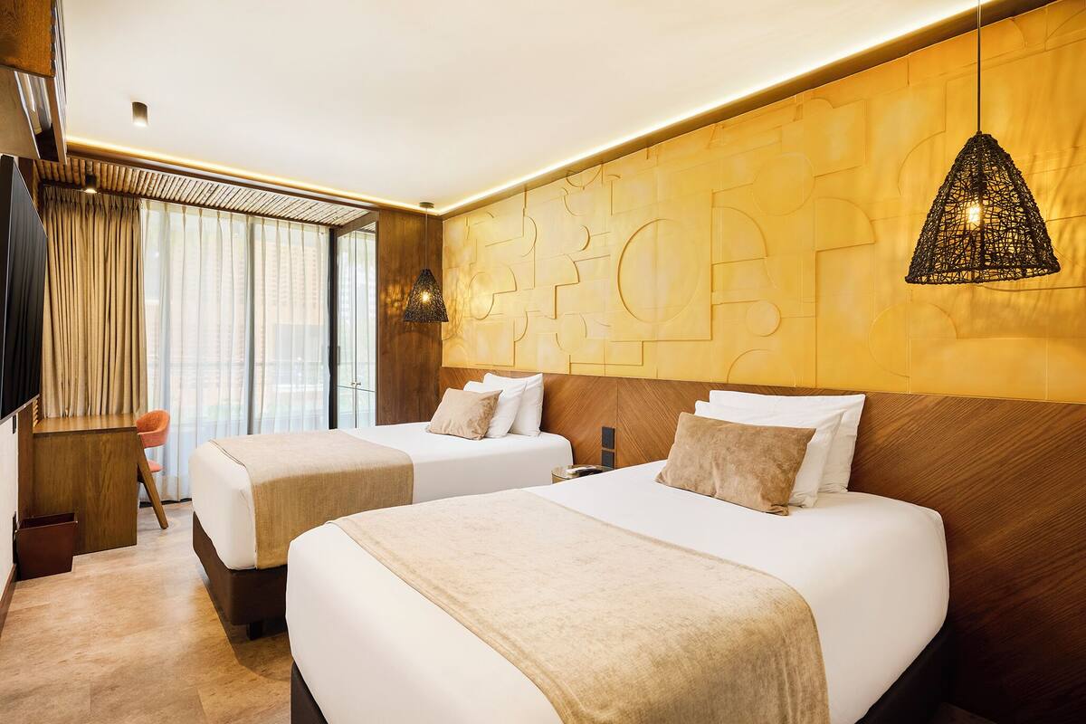 A hotel room with two beds, a desk, and a TV.