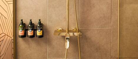 A shower with a handheld showerhead, a wall-mounted control panel, and three bottles of shampoo on the wall.