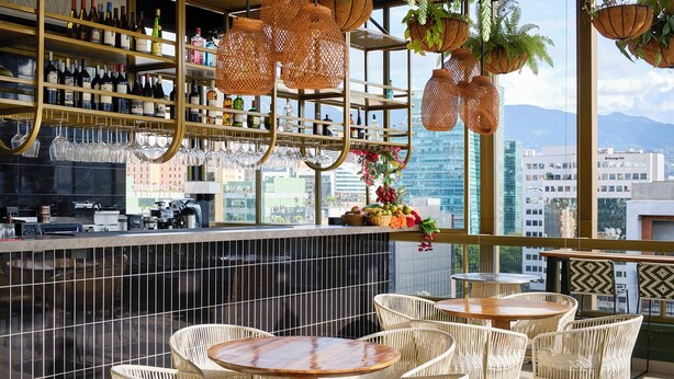 A bar area with wicker furniture, shelves with bottles, and a city view. - Golden Valley Hotel (Medellín)