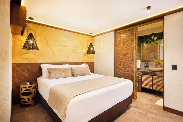 Un dormitorio moderno con una cama grande, dos lámparas colgantes, un cabecero de madera, una mesita de noche y un baño con lavamanos y espejo.