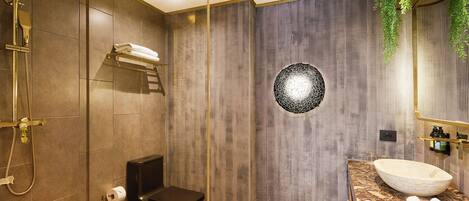A modern bathroom with a large mirror, a round sink, and a shower area.