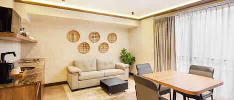 A modern living room with a sofa, a dining table, chairs, a coffee table, a kitchen area with a microwave, and decorative wall art.