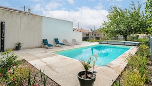 A swimming pool with lounge chairs, a potted plant, and a white wall.