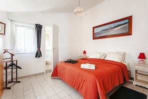 Une chambre à coucher avec un lit, une table de chevet, une lampe, un tableau au mur et une fenêtre avec des rideaux.
