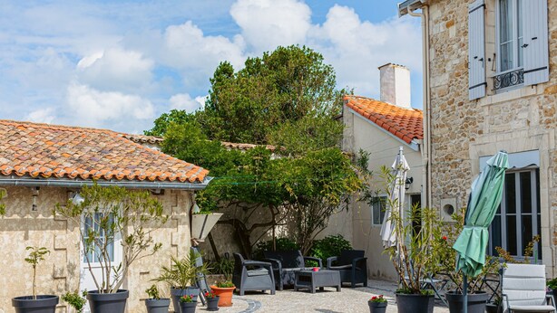 A cobblestone courtyard with outdoor furniture, potted plants, and stone buildings.
