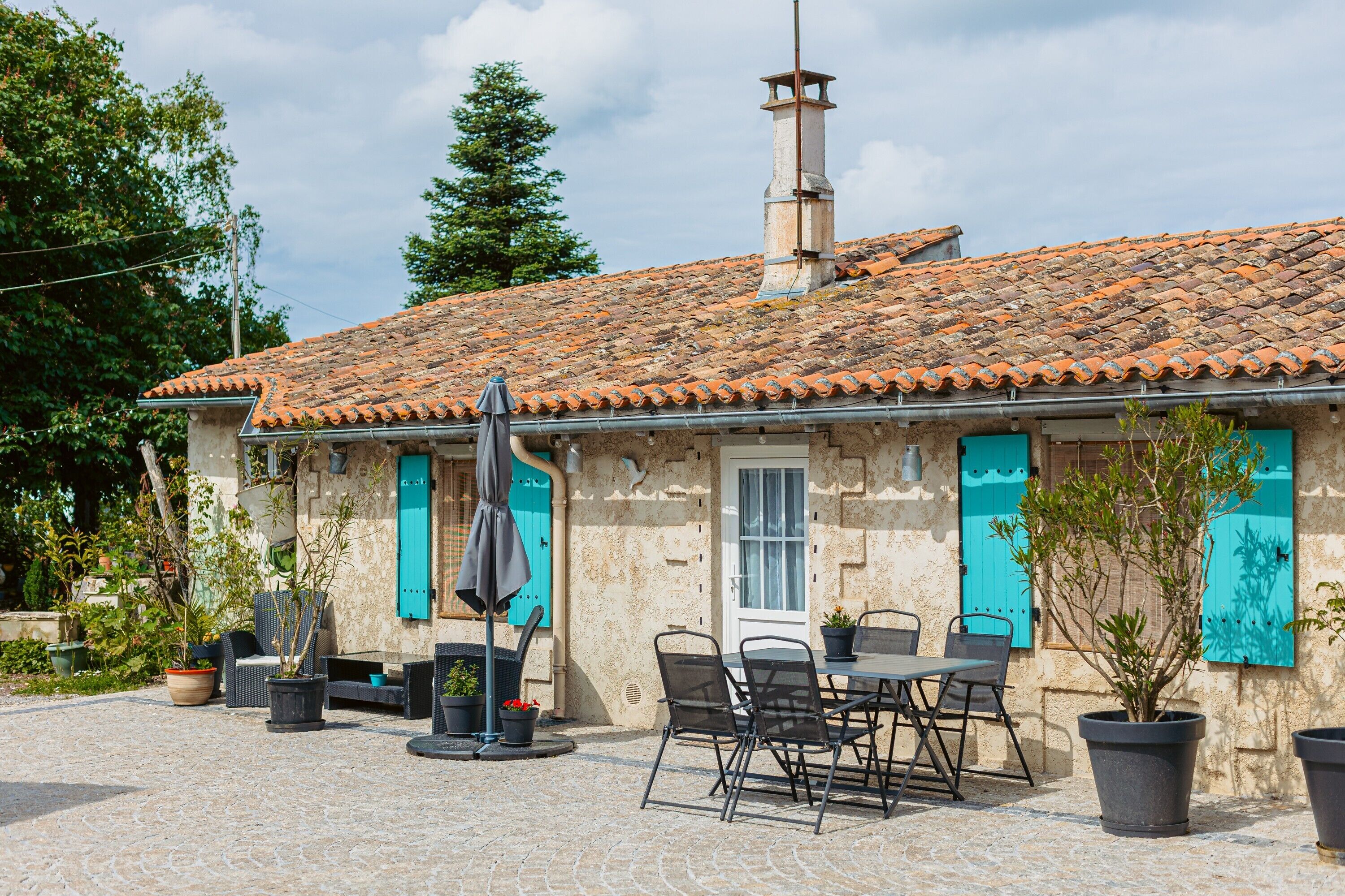 A stone building with a tiled roof, outdoor seating, and potted plants.