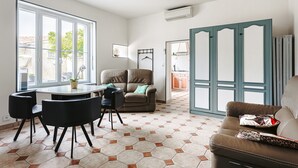 A spacious living area with a dining table, chairs, a sofa, and a large window.