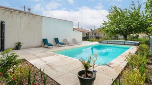 A swimming pool with lounge chairs, a potted plant, and a white wall.