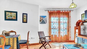 Une pièce comprenant une table à manger, des chaises, un téléviseur et une fenêtre avec des rideaux.