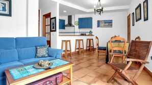 Un salon avec un canapé bleu, une table basse en bois et un coin repas comprenant des tabourets et une chaise en bois.