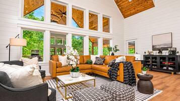A spacious living room with a high ceiling, large windows, and a modern fireplace.