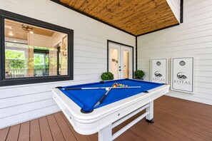 A pool table with balls on a wooden deck, surrounded by white walls and a wooden ceiling.