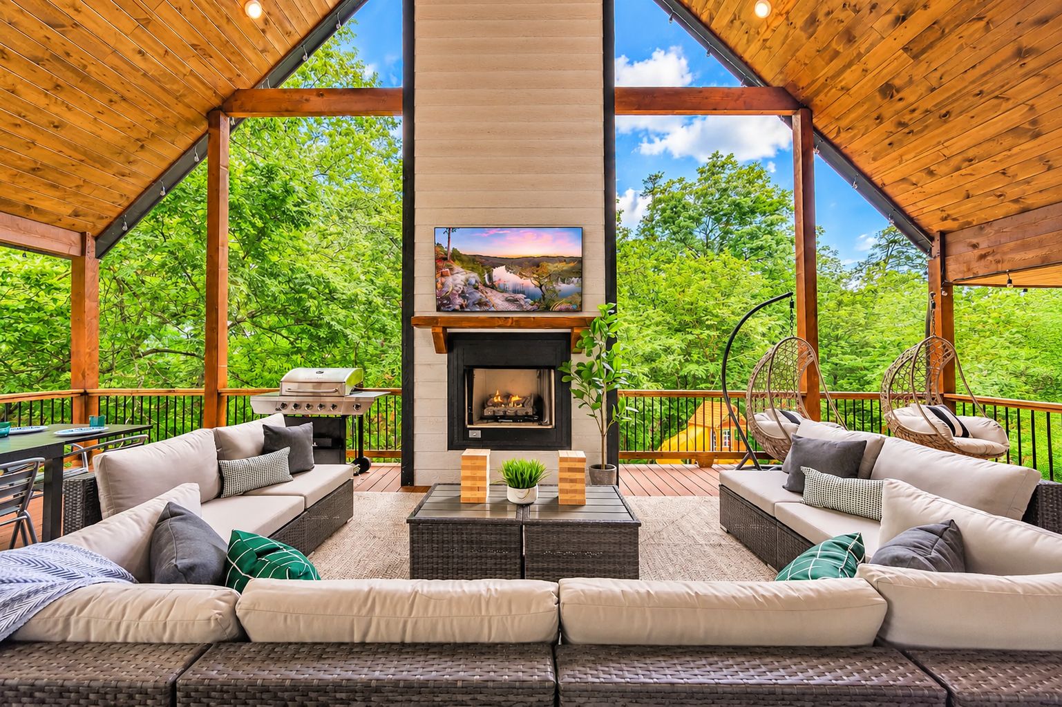 A spacious outdoor living area with a fireplace, comfortable seating, and a view of lush greenery.