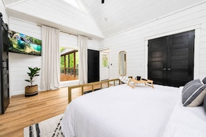 A bedroom with a large bed, a TV, a wooden bench, and a view of the outdoors. - Swim Spa & Game-Loaded Family Cabin | Sleeps 14 (Broken Bow)