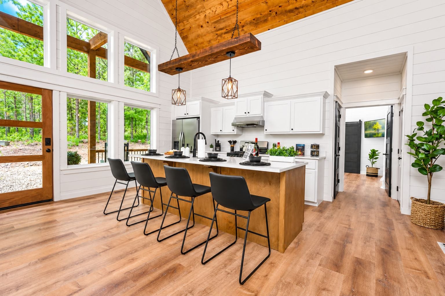 A modern kitchen with a large island, black bar stools, and wooden flooring.