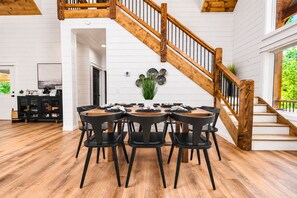 A dining area with a wooden staircase, a dining table with chairs, and a kitchen area in the background.