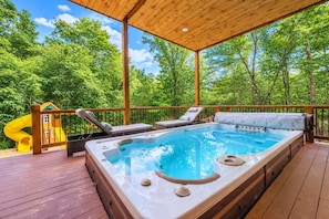 A hot tub on a wooden deck with a slide, surrounded by trees. - Swim Spa & Game-Loaded Family Cabin | Sleeps 14 (Broken Bow)
