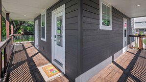 Un portico coperto con un patio in legno, una porta bianca e una finestra.