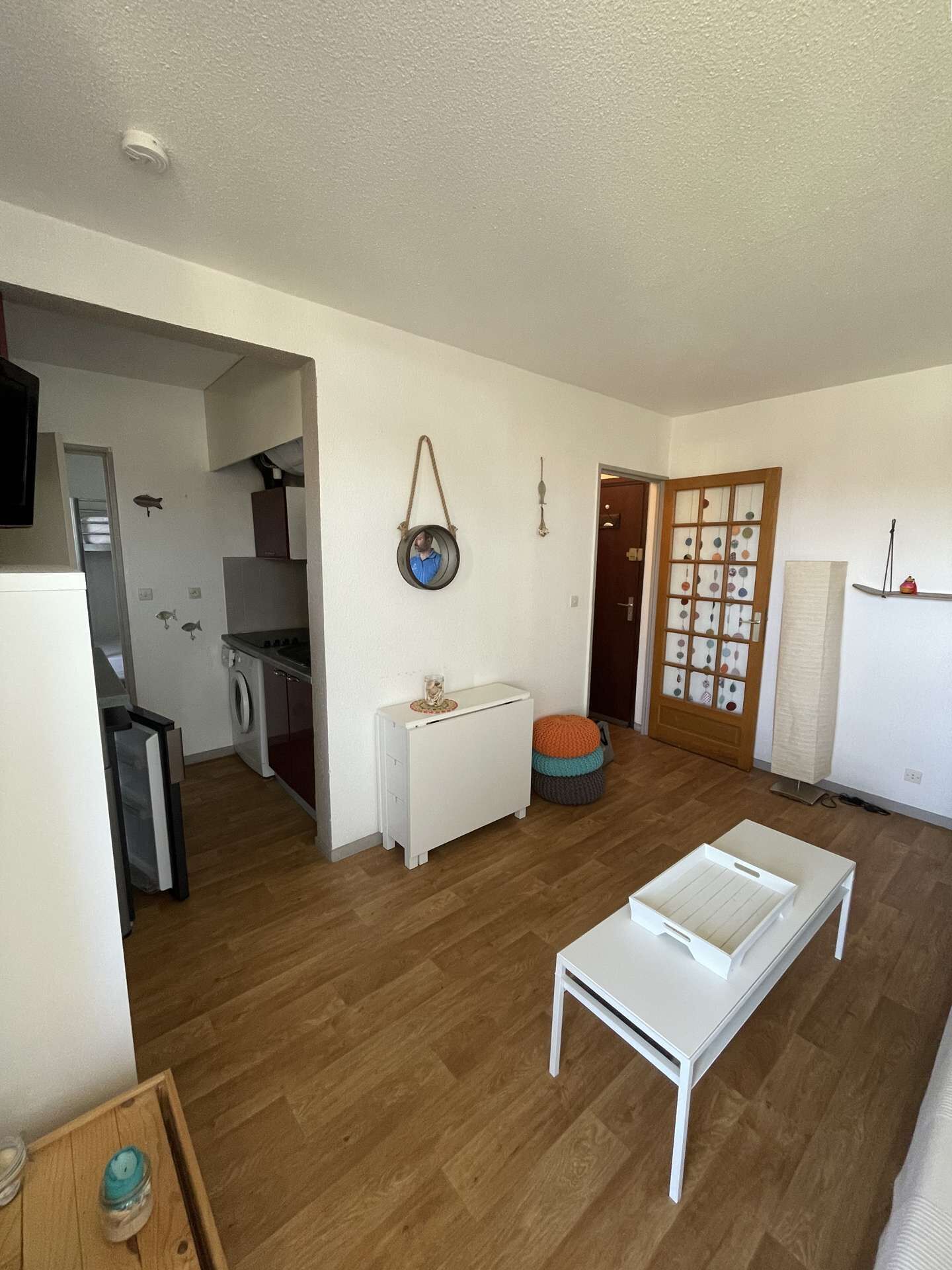 A spacious living area with a wooden floor, a white sofa, a small white table, and a kitchen in the background.