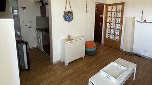 A spacious living area with a wooden floor, a white sofa, a small white table, and a kitchen in the background.