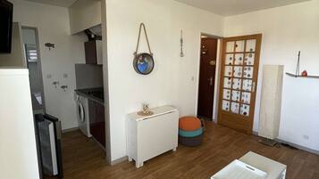 A spacious living area with a wooden floor, a white sofa, a small white table, and a kitchen in the background.